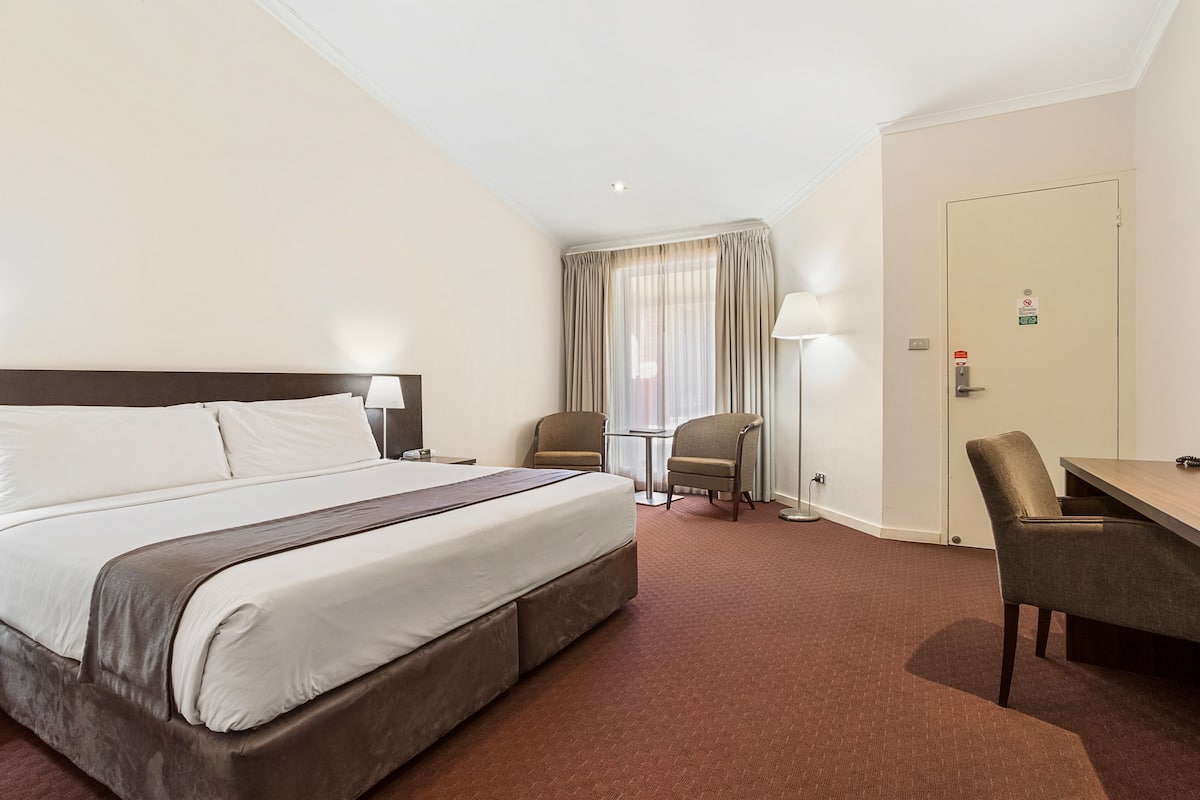 A hotel room with a large bed, two chairs, a small table, and a desk.