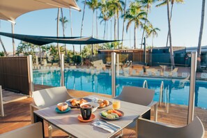 A dining table with breakfast items and a view of a swimming pool with palm trees. - Karratha International Hotel (Pegs Creek)