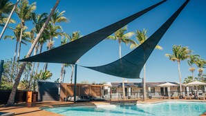 Un espace piscine doté d’une terrasse en bois, de chaises longues et de palmiers.