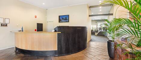 A reception area with a curved counter, a large potted plant, and a staircase leading to an upper level.