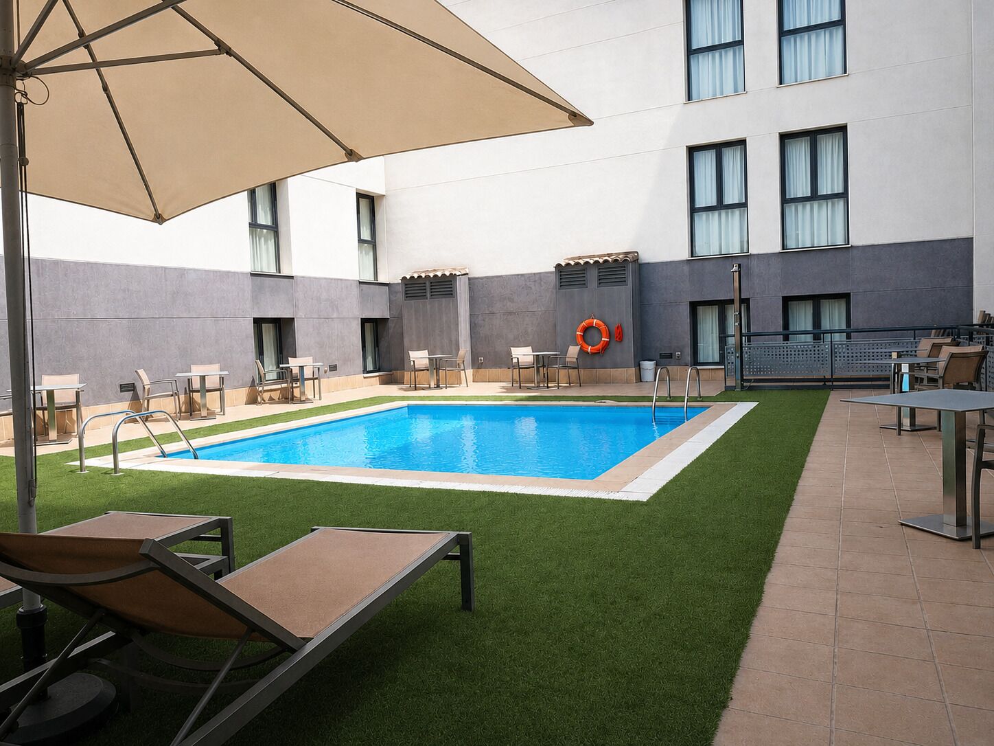 A swimming pool with a lifebuoy, outdoor seating, and a building with large windows.