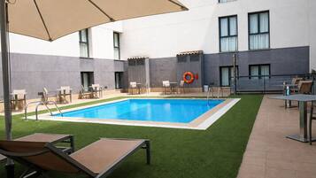 A swimming pool with a lifebuoy, outdoor seating, and a building with large windows.