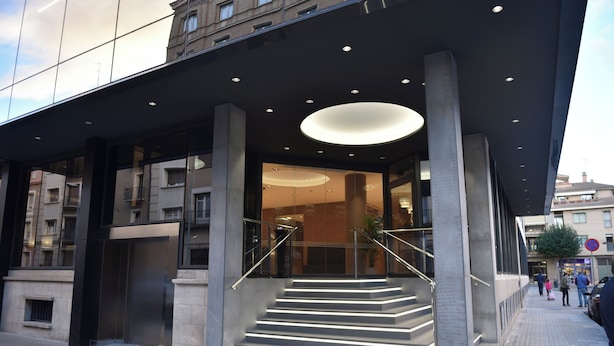 A modern building entrance with a glass facade, a staircase, and a circular light fixture above the entrance.