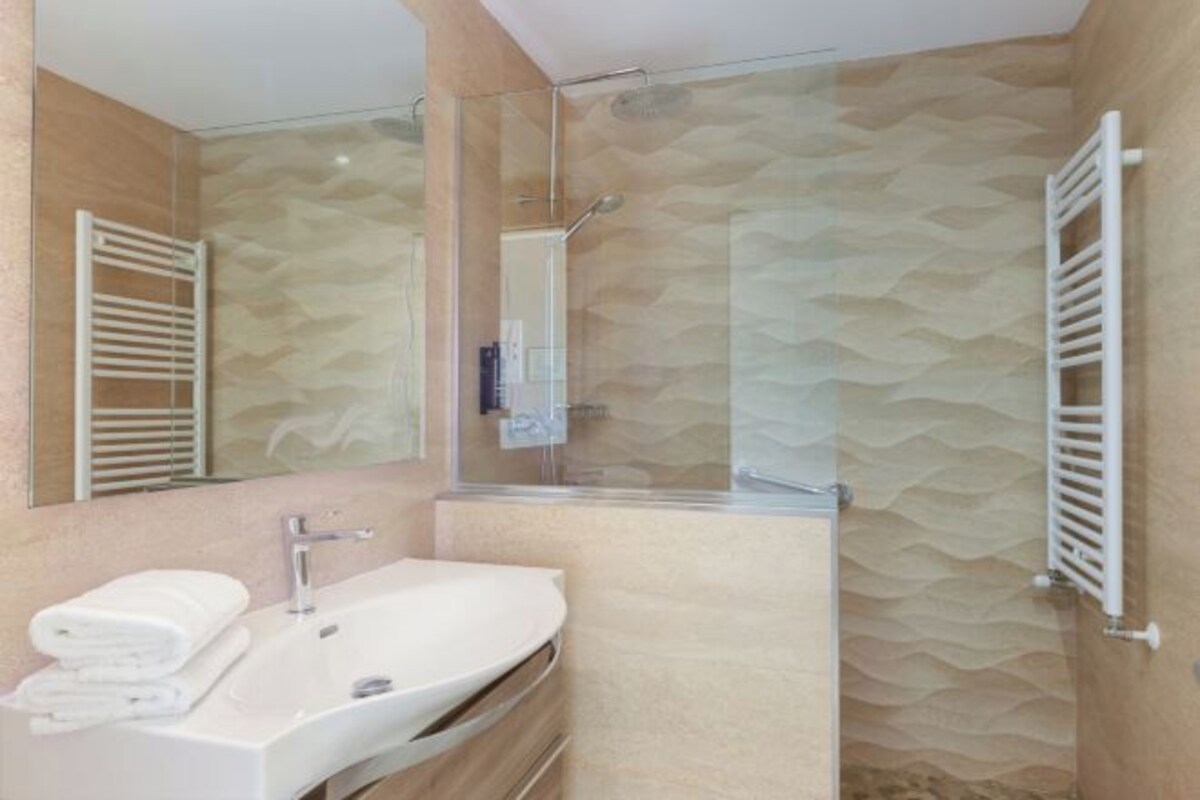 Un baño con un lavamanos moderno, cabina de ducha de vidrio y pared con textura.
