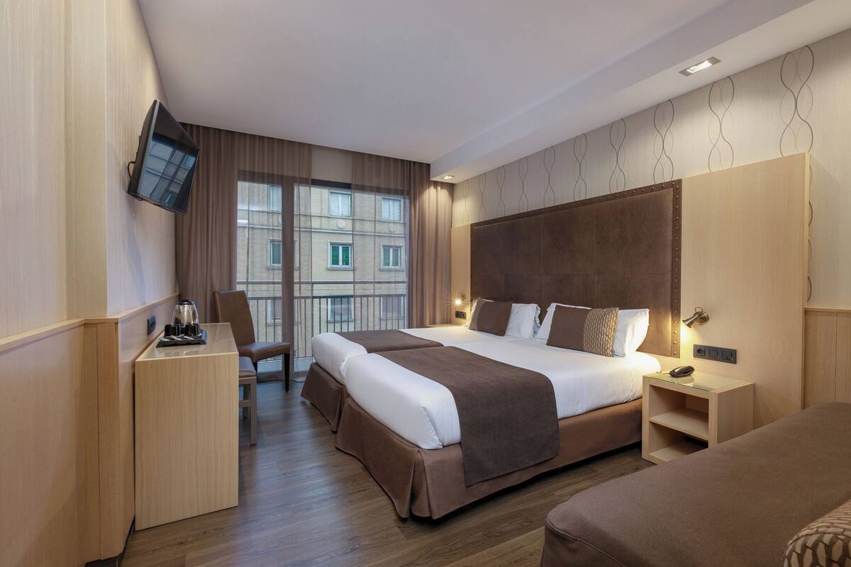 A modern hotel room with a large bed, a desk, and a TV mounted on the wall.