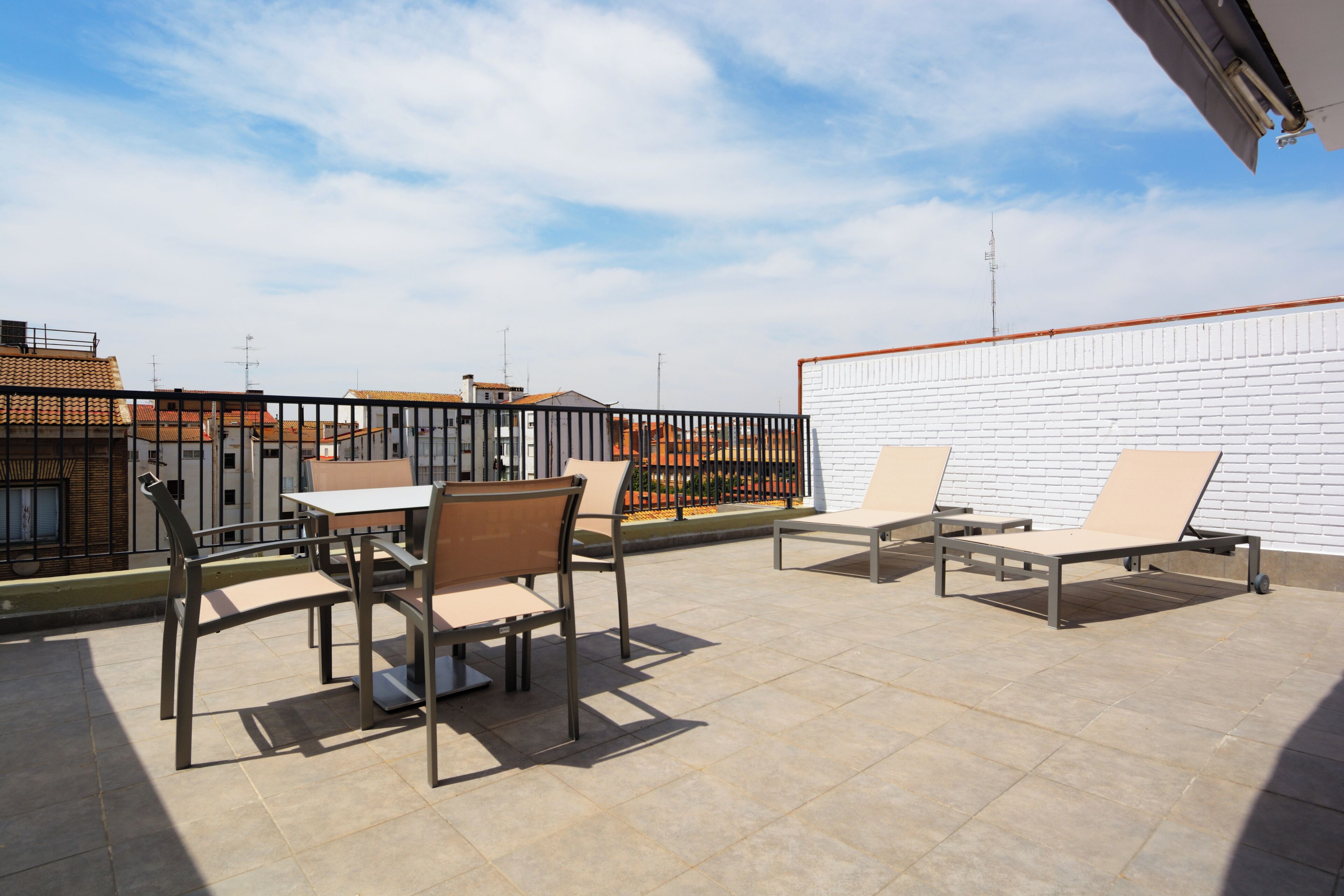 Une terrasse sur le toit, avec une table et des chaises, un mur en briques blanches et une vue sur les bâtiments en arrière-plan.