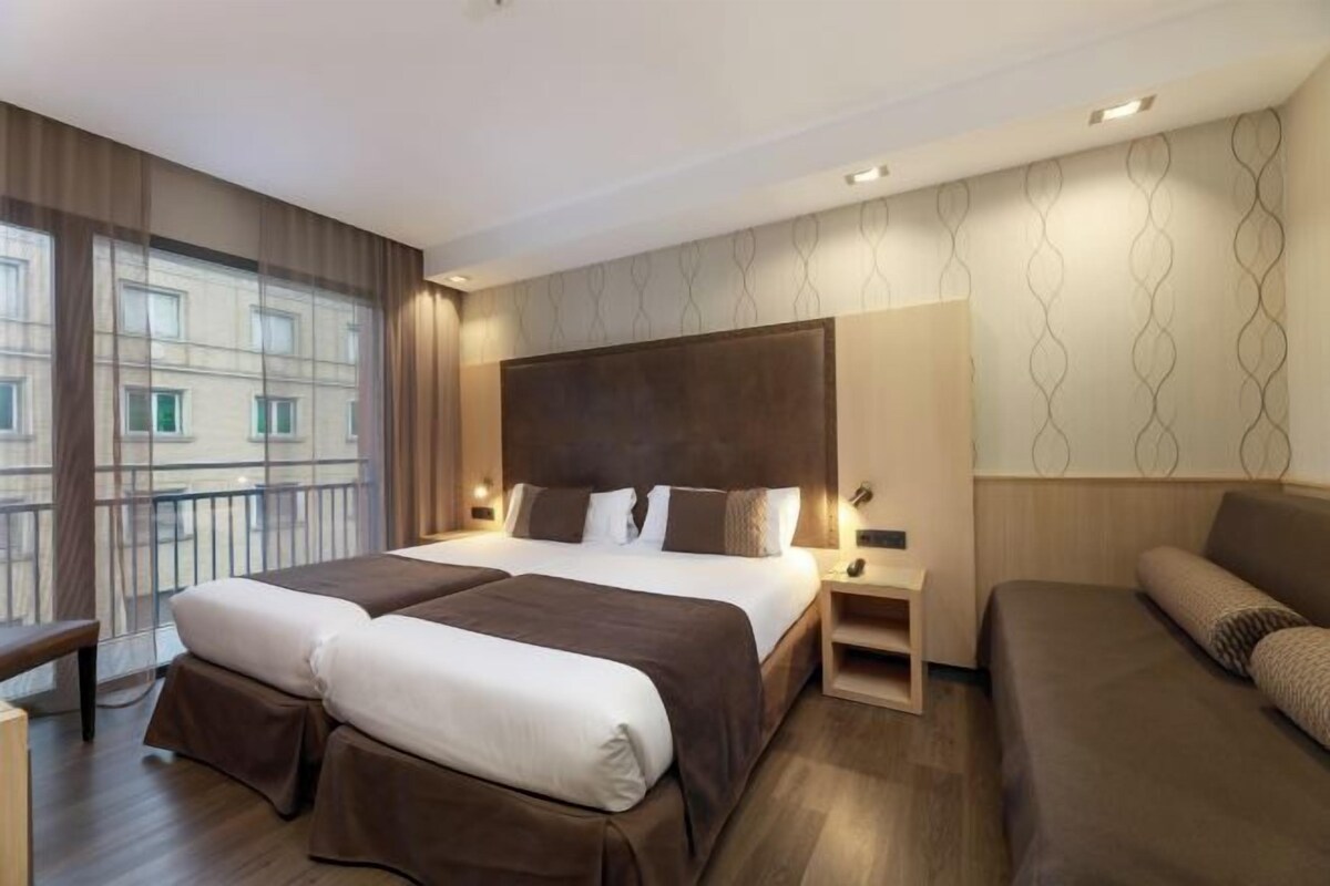 A modern hotel room with a large bed, a sofa, and a desk.