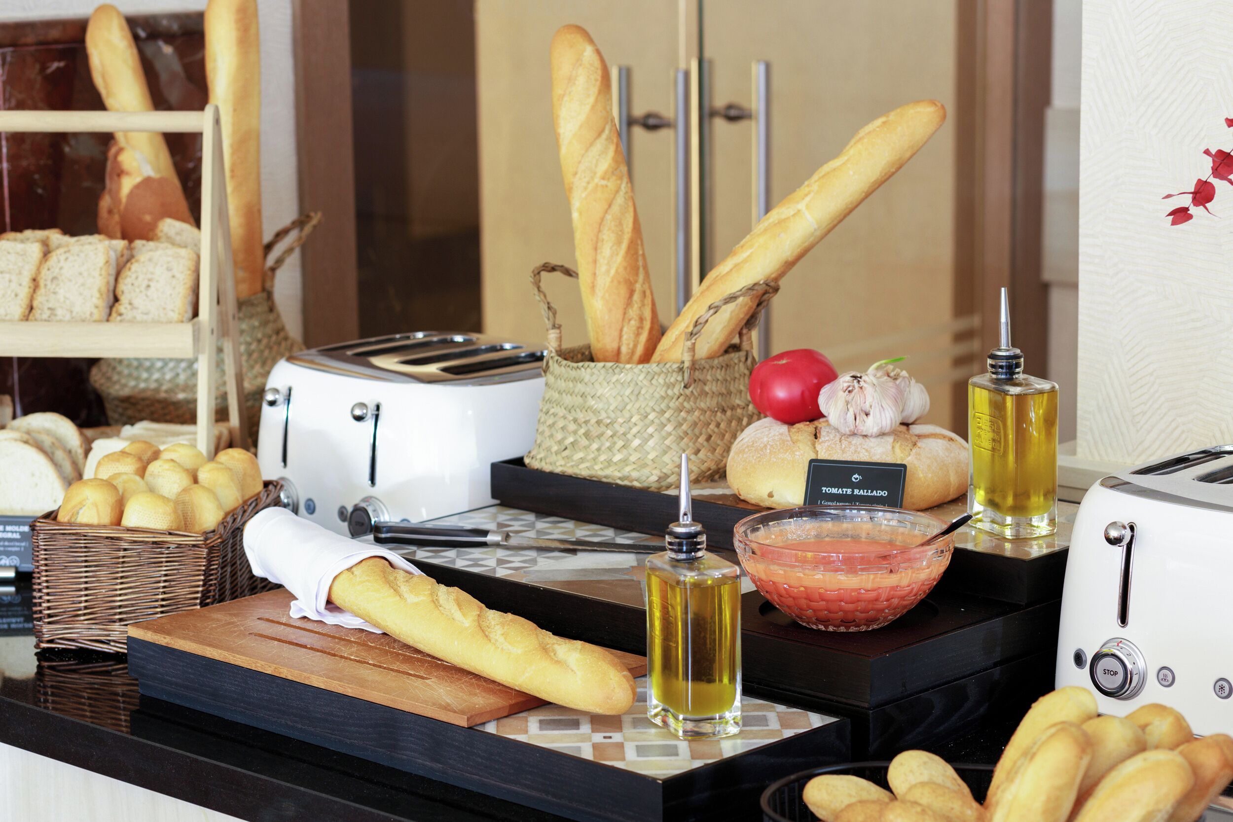 A buffet counter with various breads, a toaster, a bowl of salad, and a bottle of oil.