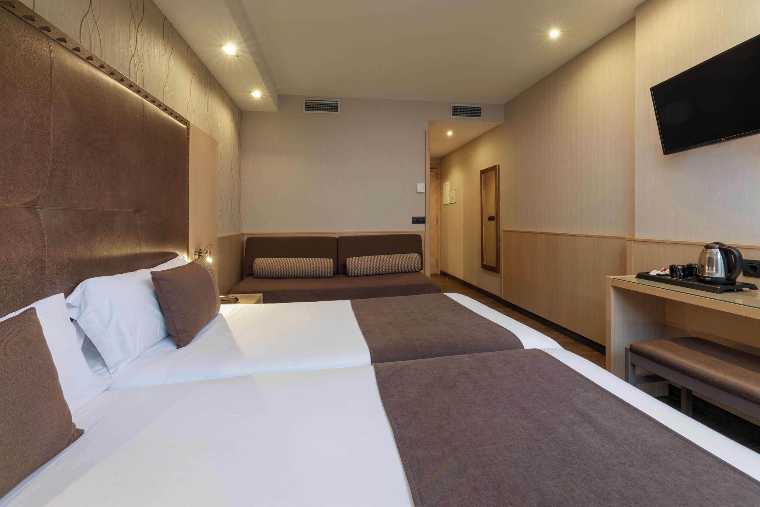 A hotel room with a large bed, a sofa, a TV, and a coffee machine.