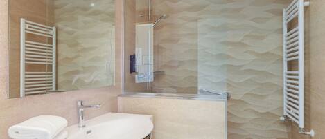 Un baño moderno con cabina de ducha de vidrio, un lavamanos blanco y un perchero para toallas.