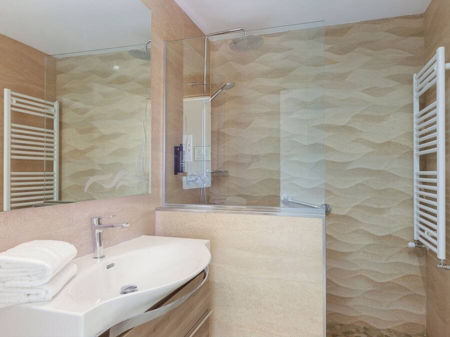 A modern bathroom with a glass shower enclosure, a white sink, and a towel rack.