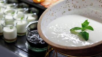 A bowl of white soup garnished with mint leaves, surrounded by various food items and small glasses.