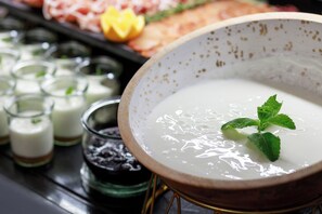 Un tazón de sopa blanca adornado con hojas de menta, rodeado de diversos alimentos y pequeños vasos.