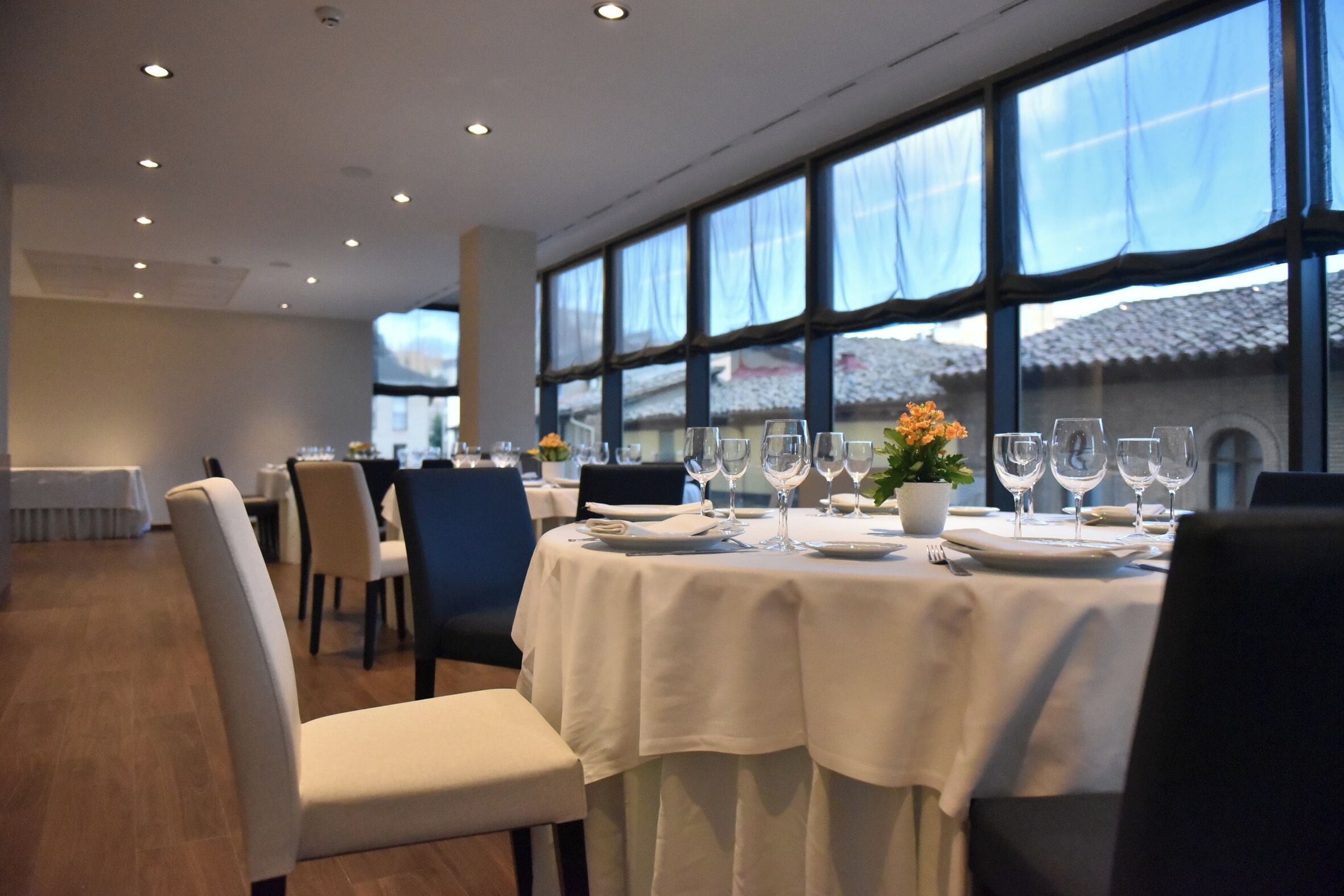 A dining area with tables set for a meal, large windows, and a view of a building outside.