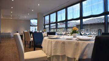 A dining area with tables set for a meal, large windows, and a view of a building outside.
