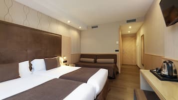 A hotel room with two beds, a desk with a kettle, and a TV mounted on the wall.