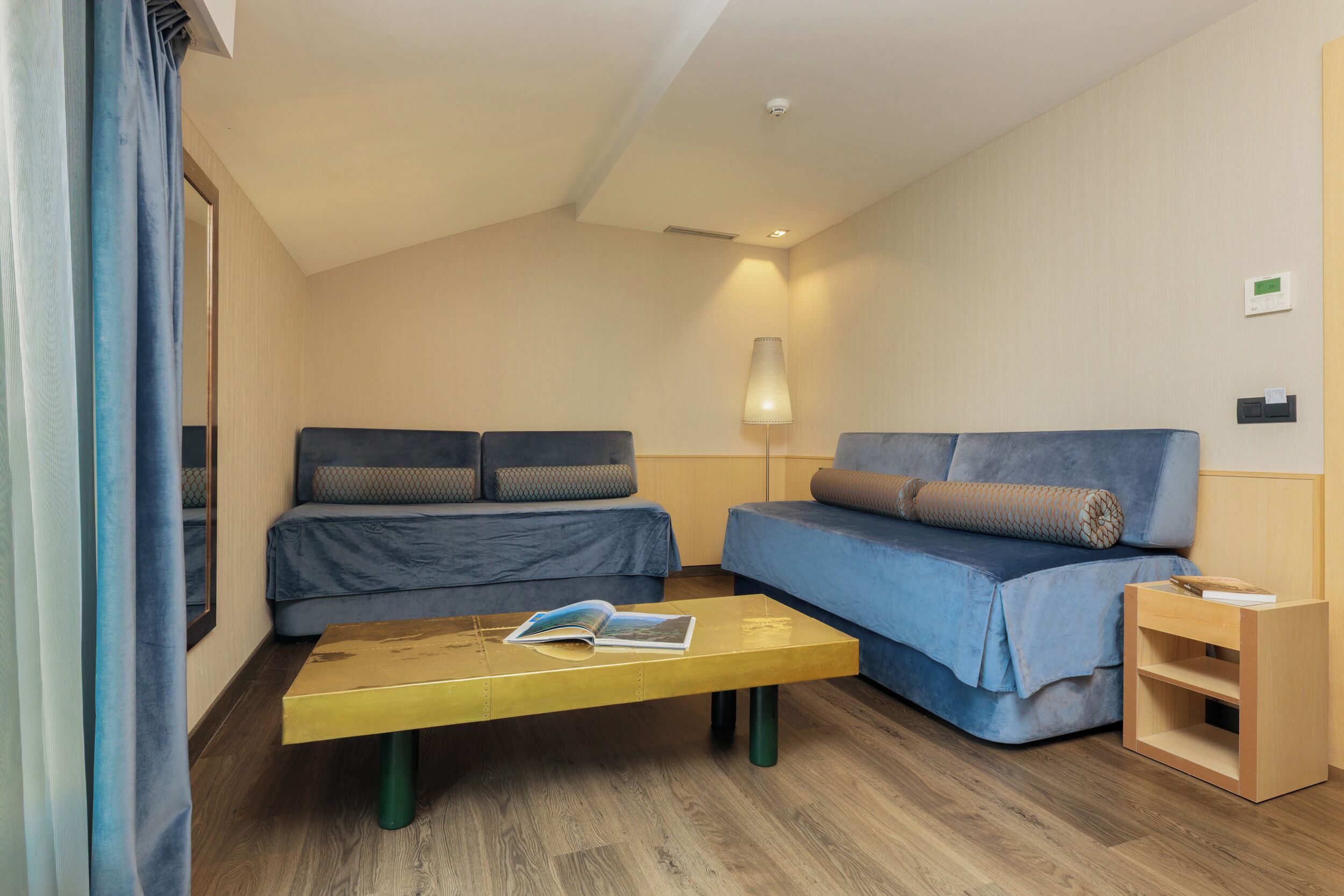 Una habitación de hotel moderna con un sofá, una mesita con un libro y una lámpara.