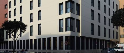 A modern building with a flat facade, multiple windows, and a corner entrance.