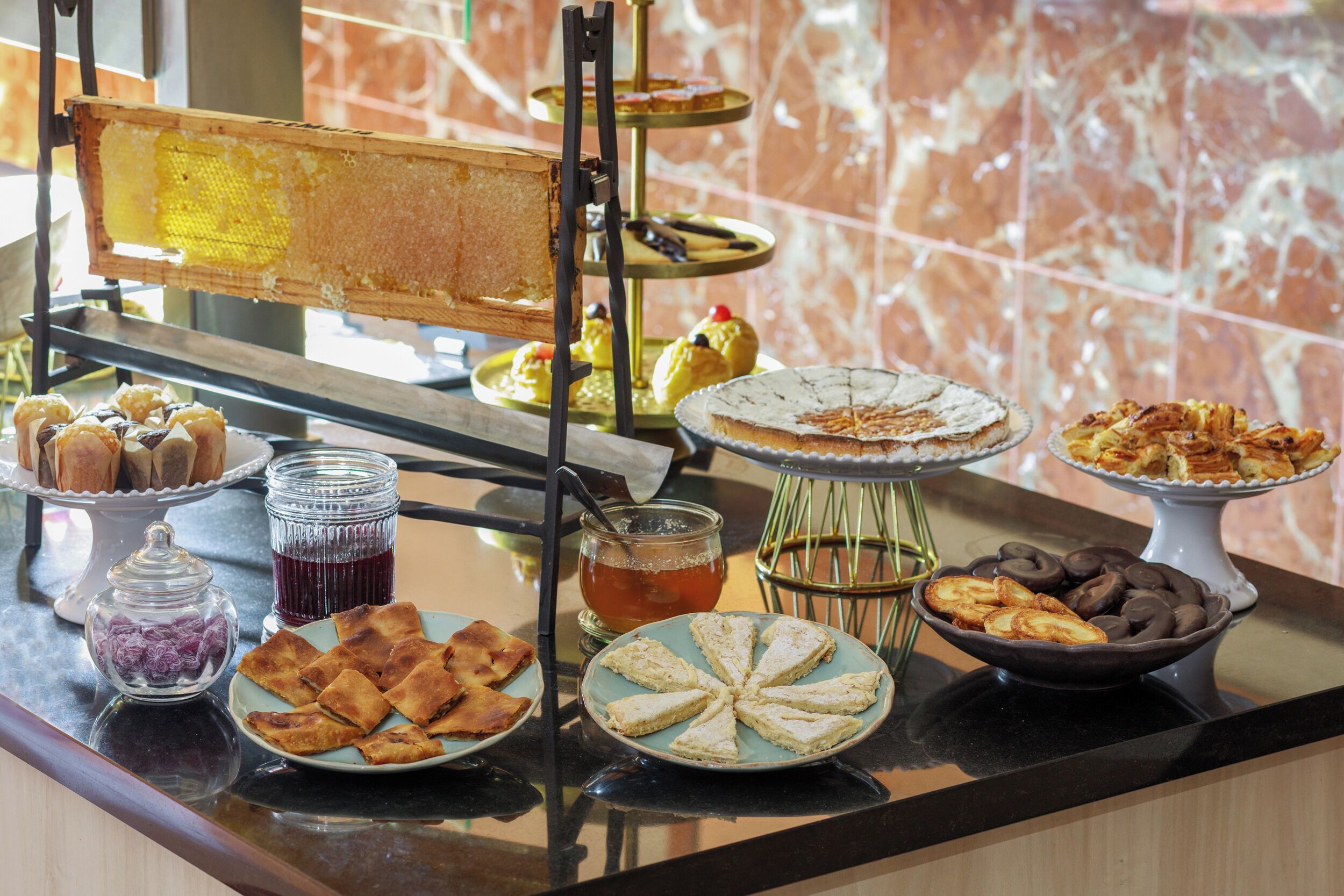 Una mesa de buffet con diversos postres y pasteles, incluyendo panales de miel, tartas y productos cubiertos de chocolate.