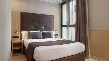 A modern hotel room with a large bed, a nightstand, a wall-mounted light, and a window with curtains.