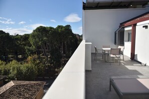 Un balcón con vistas a árboles y un edificio blanco. Hay dos sillas y una mesa en el balcón.