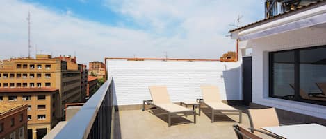 Una terraza en la azotea con tumbonas, una mesa y vistas panorámicas de la ciudad.