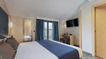 A hotel room with a large bed, a desk with a chair, a flat-screen TV, and a sliding glass door to the balcony.