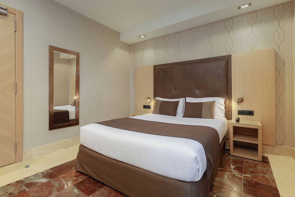 A hotel room with a large bed, a wooden headboard, a nightstand, a mirror, and a wardrobe.