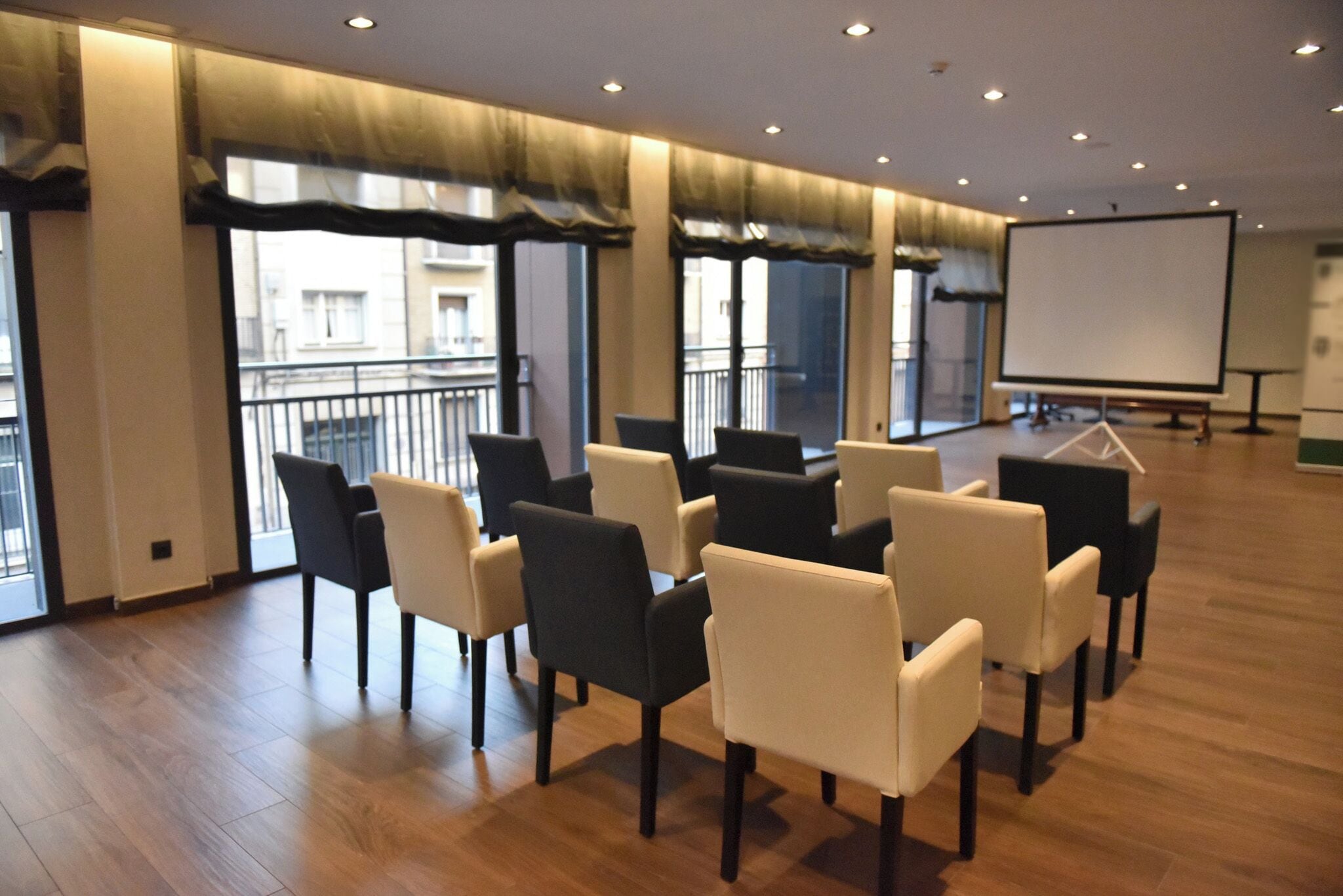 Un salón de conferencias con una pizarra, varias sillas y ventanas amplias con cortinas.
