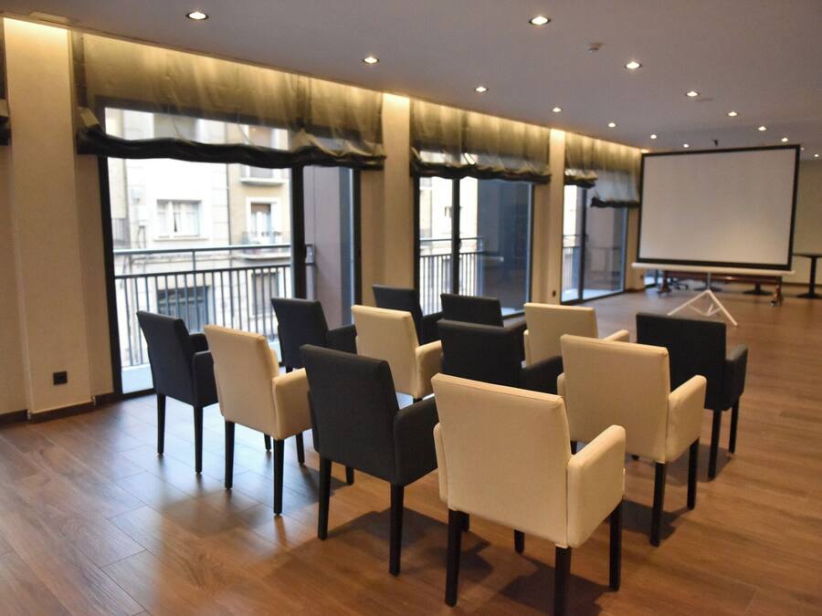 Ein Konferenzraum mit einer Wandtafel, mehreren Stühlen und großen Fenstern mit Vorhängen.