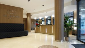 A hotel reception area with a reception desk, a sofa, and a potted plant.