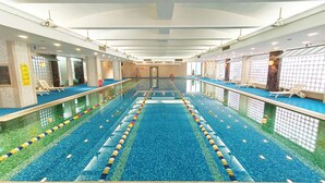 En stor inomhuspool med flera banor, solstolar och ett tak med infälld belysning.