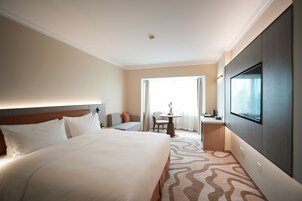 Habitación de hotel con una cama grande, un sofá, una mesita de noche con un florero y un televisor en la pared.