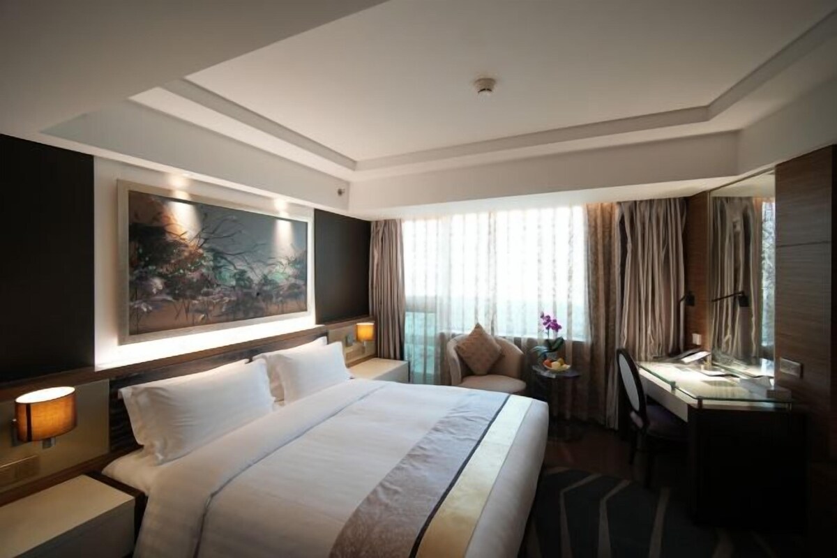 A hotel room with a large bed, a desk, a chair, and a window with curtains.