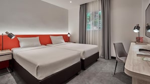 Hotellihuone, jossa on kaksi sänkyä, työpöytä, tuoli, lamppu ja ikkuna, jossa on verhot.