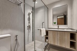 Un baño moderno con ducha envuelta en vidrio, tocador de madera y un espejo grande.