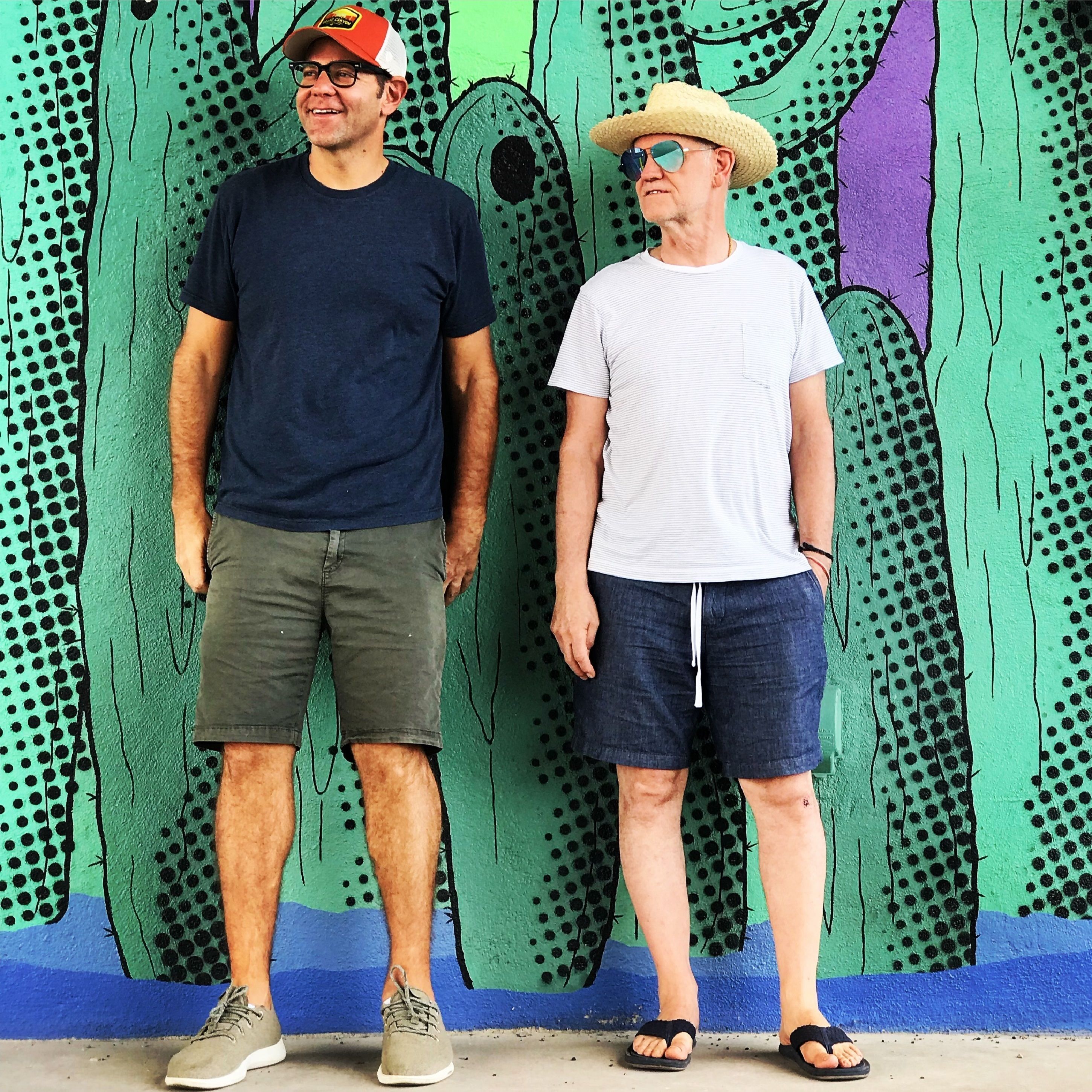 Dos hombres de pie frente a una pared con diseño de cactus.