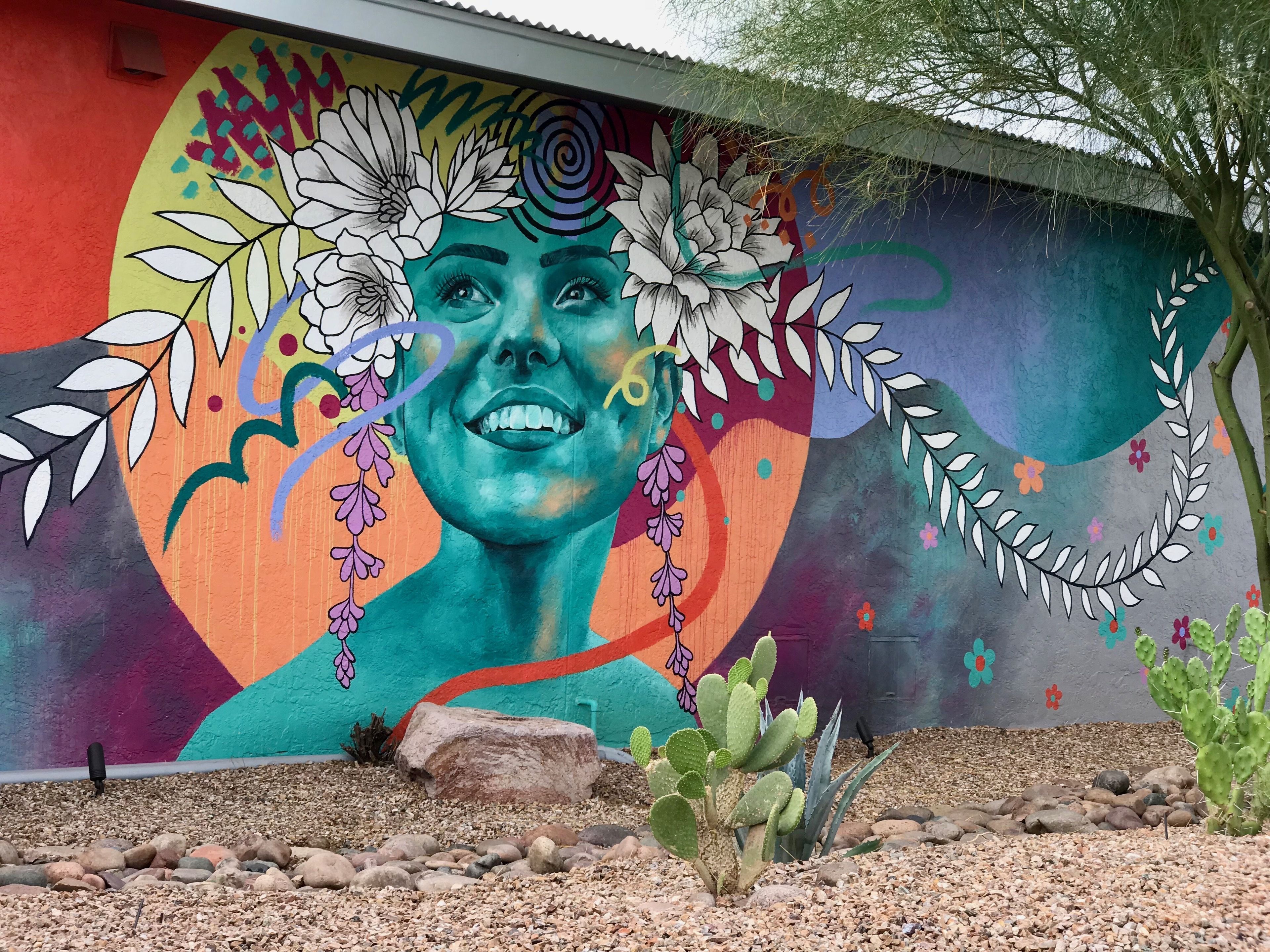 A mural with a woman's face, flowers, and a cactus garden in front.