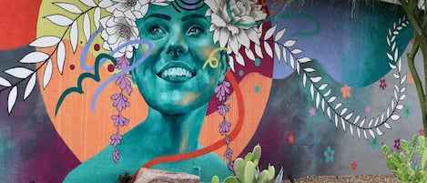 A mural with a woman's face, flowers, and a cactus garden in front.