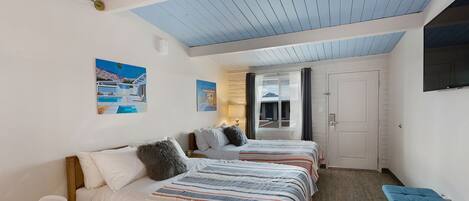 A bedroom with two beds, a bench, a TV, and a door leading to a balcony.