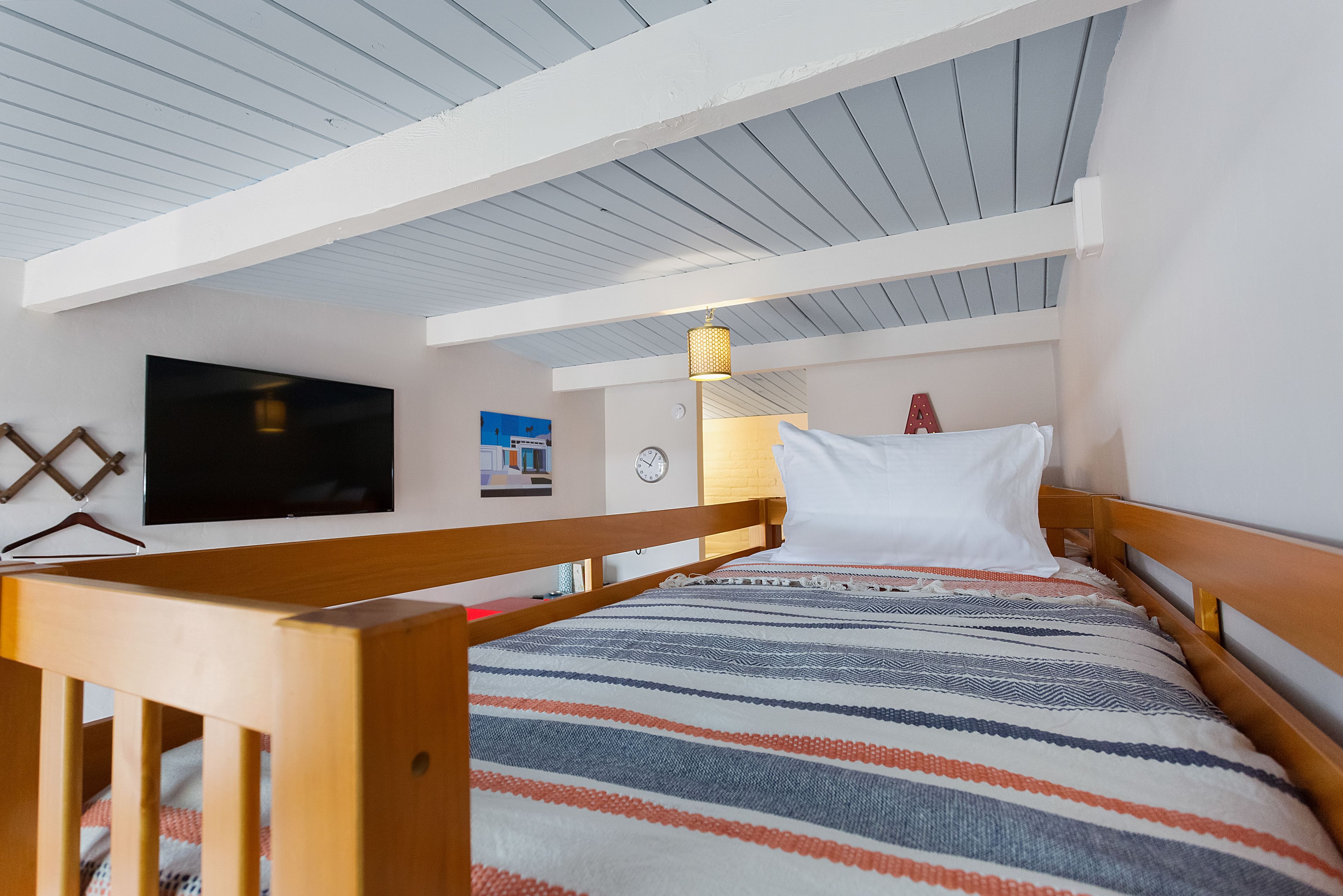 A bedroom with a bed, wooden headboard, a television mounted on the wall, a clock, and a lamp.