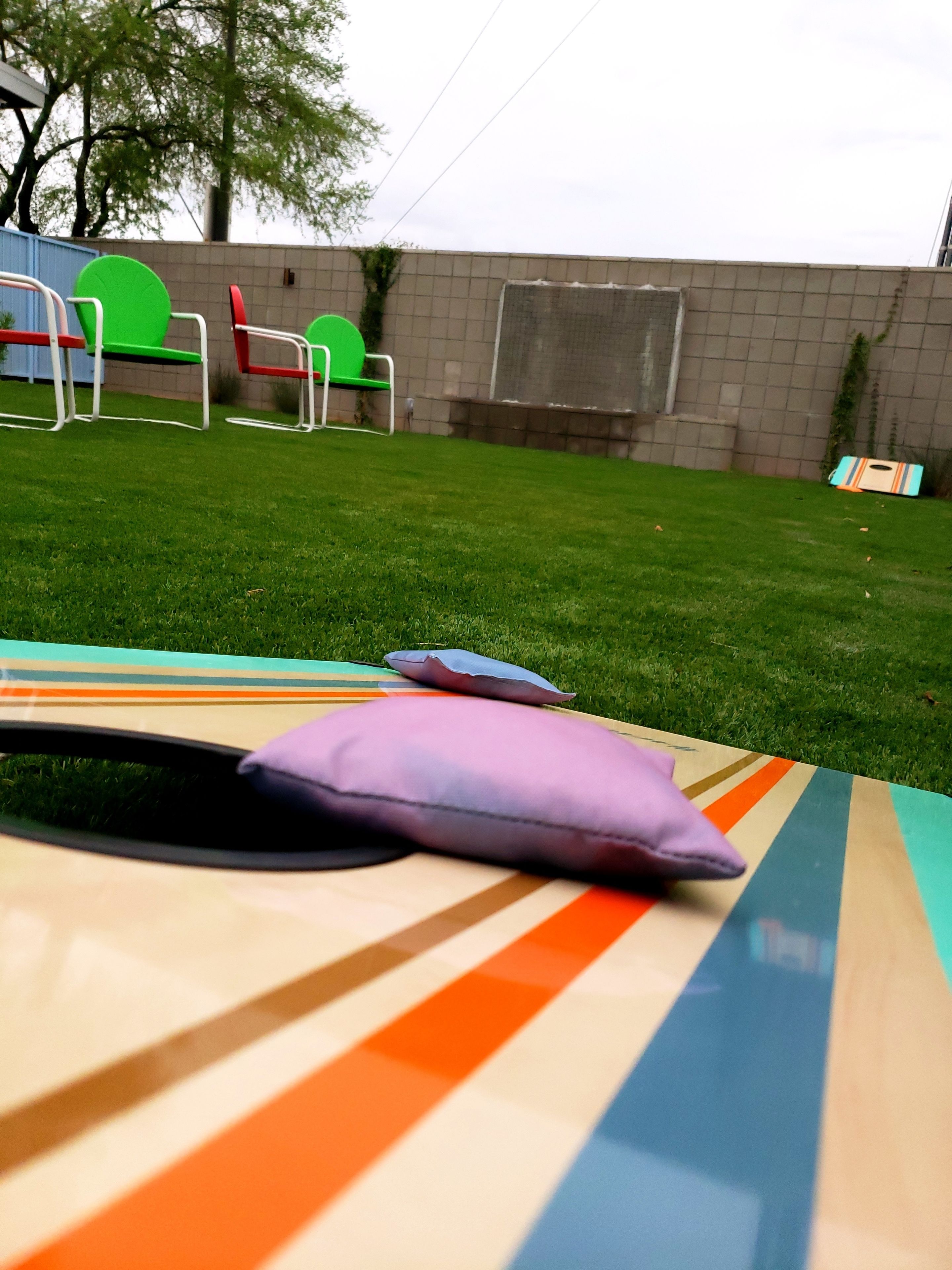 Une table rayée aux couleurs vives, sur laquelle est posé un coussin violet, est placée sur une pelouse verdoyante.