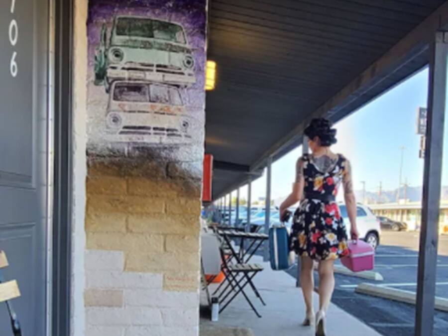 A woman walking past a building with a mural of a car on the wall.