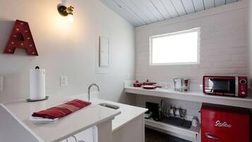 Una cocina compacta con encimera blanca, un refrigerador rojo, un microondas y una ventana sobre el fregadero.