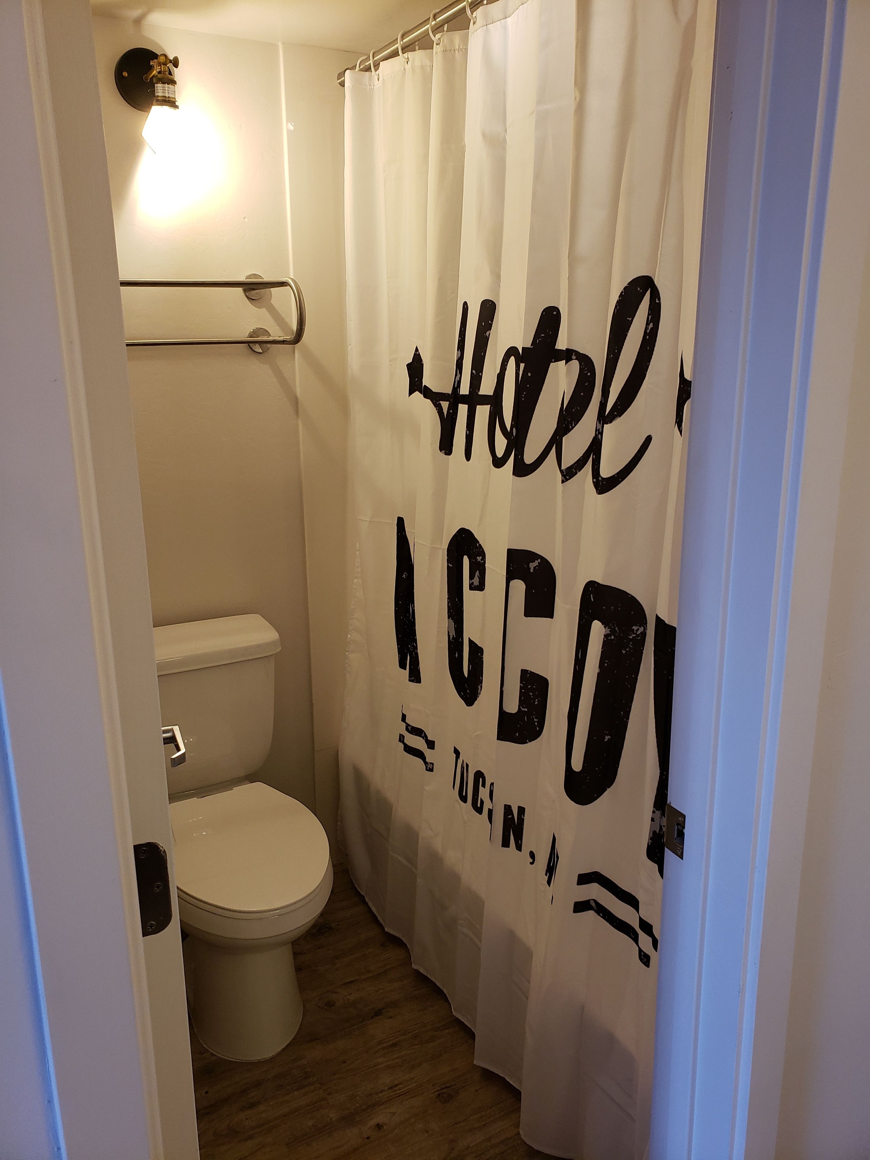Une petite salle de bain aux dimensions réduites, avec des toilettes blanches et un rideau de douche orné du texte « Hotel ACCO ».
