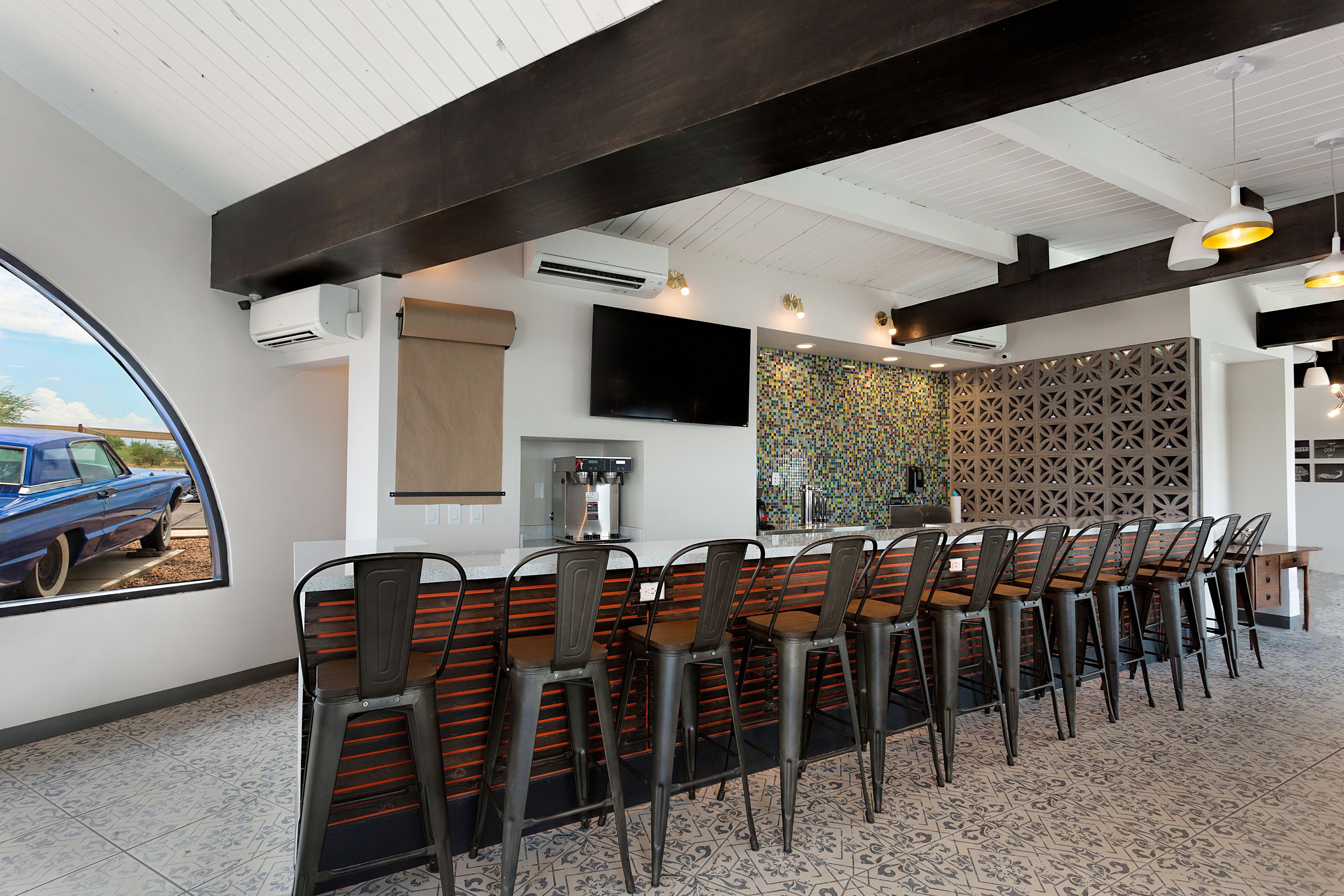 A restaurant with a long counter, multiple chairs, a TV mounted on the wall, and a decorative wall panel.
