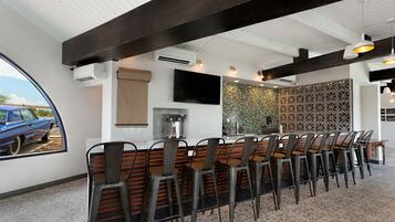 Un restaurante con una barra alargada, numerosas sillas, un televisor en la pared y un panel decorativo.