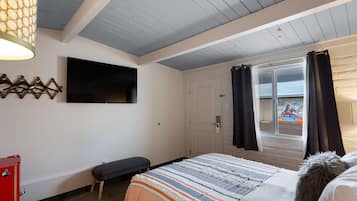 Un dormitorio con cama, un banco, un televisor y una puerta que da a un balcón.