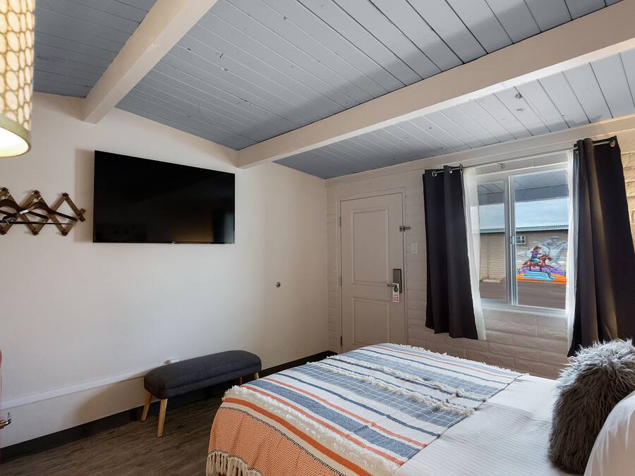 Un dormitorio con cama, un banco, un televisor y una puerta que da a un balcón.