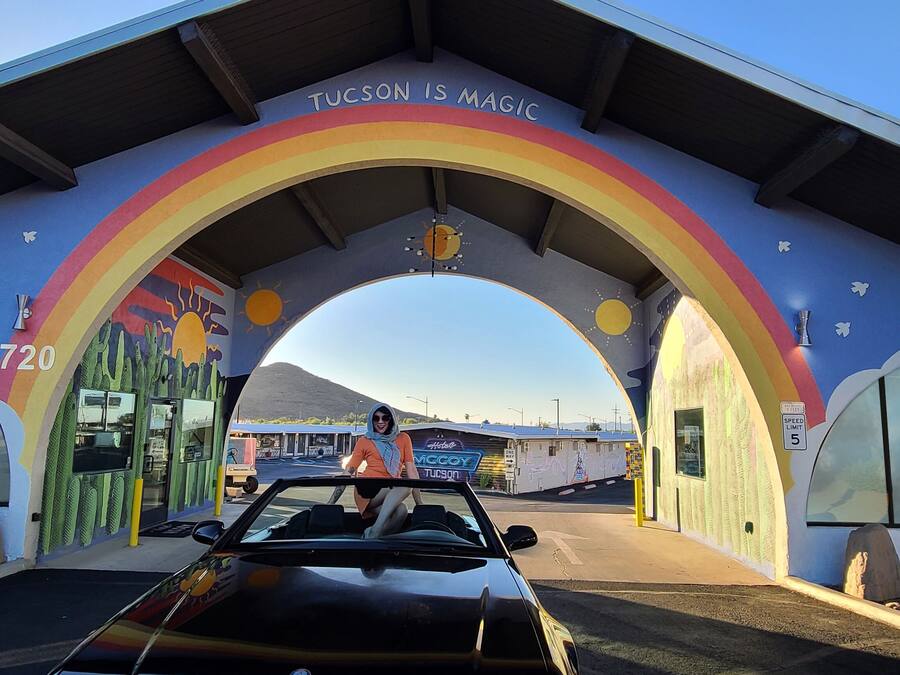 A car driving through a tunnel with a rainbow arch and the text "Tucson is Magic" on the arch.